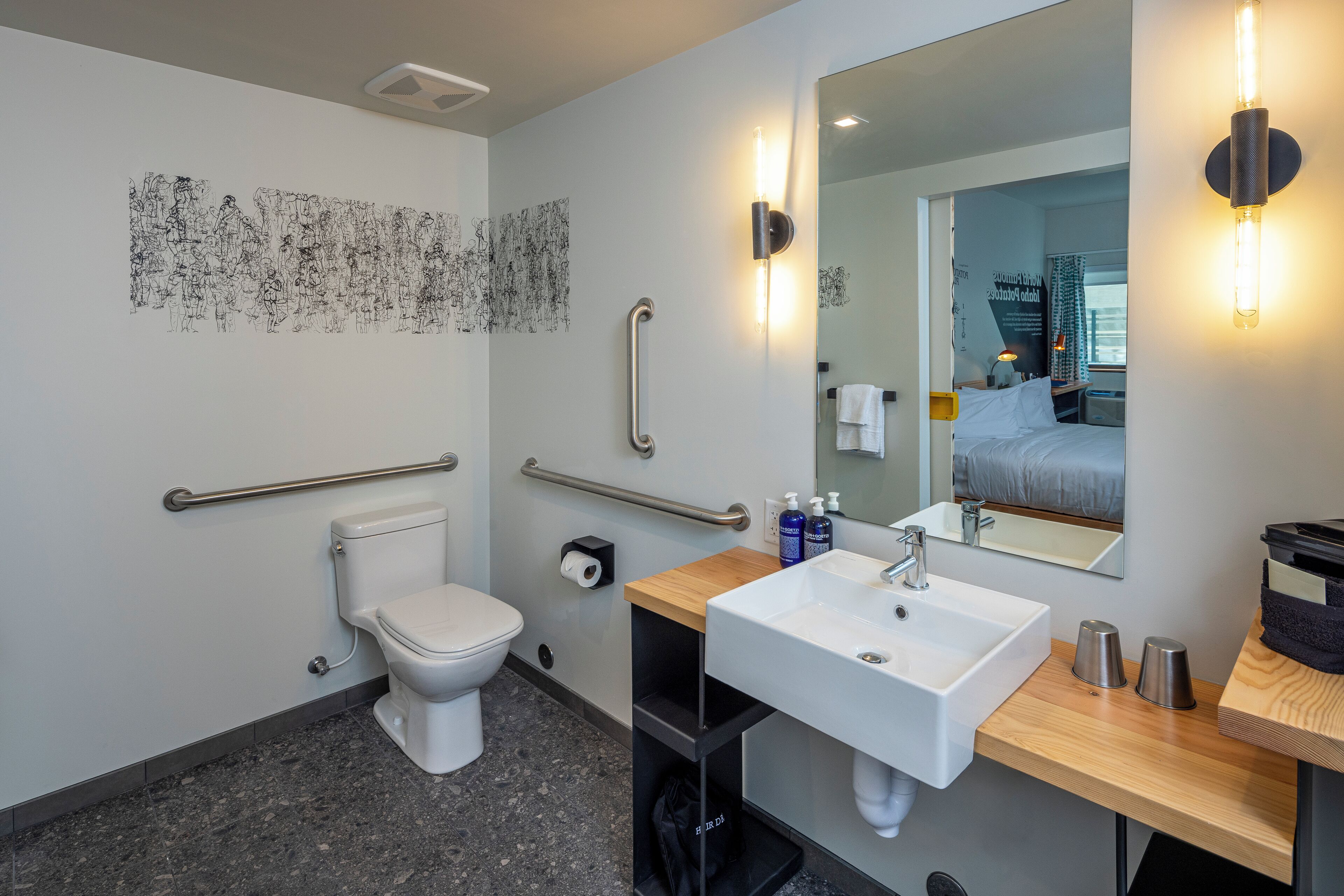 Une salle de bain moderne équipée de toilettes, d’un bidet et d’un lavabo. Elle comprend également des barres d’appui, un miroir et un porte-serviettes.