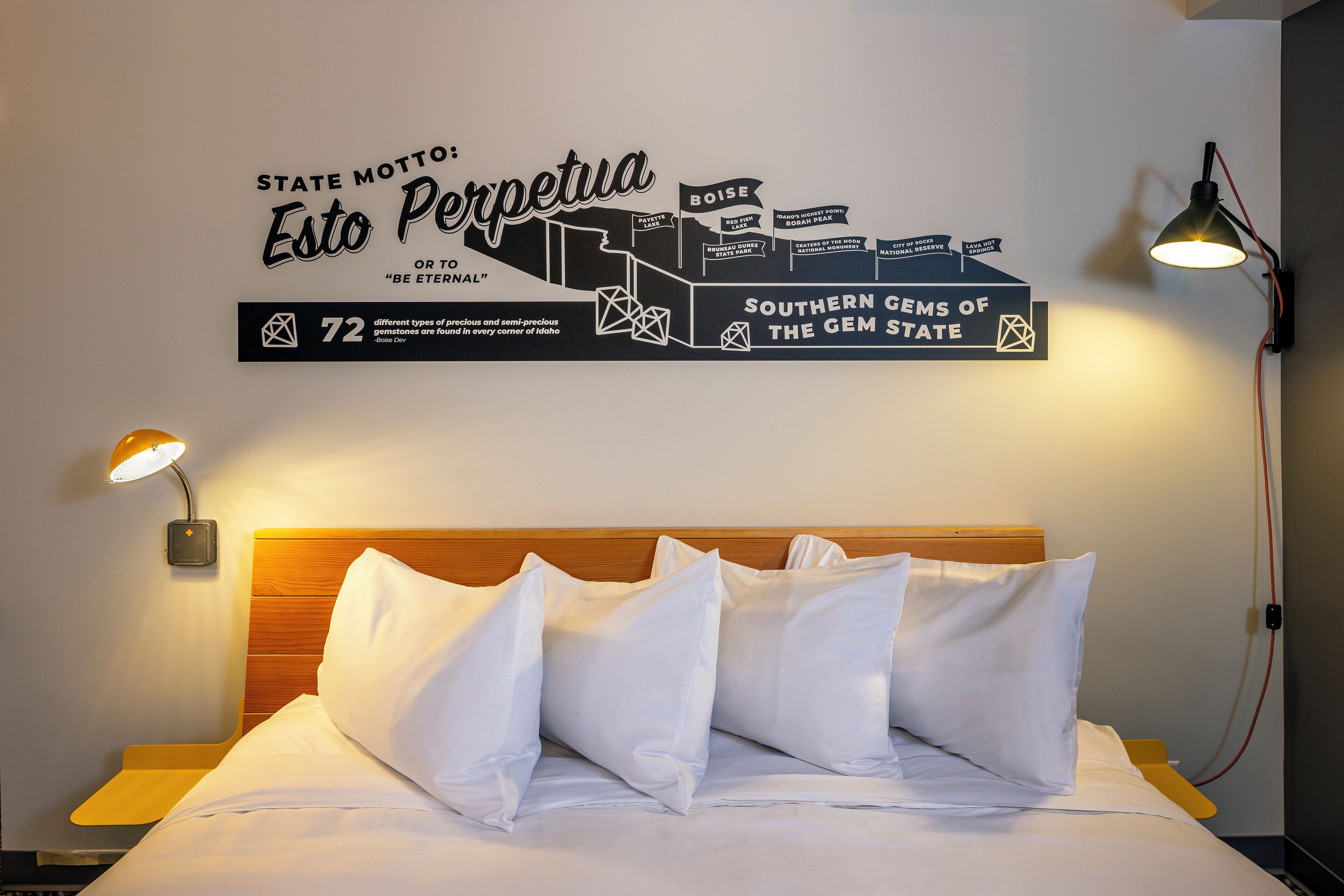 Ein Hotelzimmer mit einem Bett, Kissen, einer Wandleuchte und einem dekorativen Schild über den Edelsteinen Idahos.