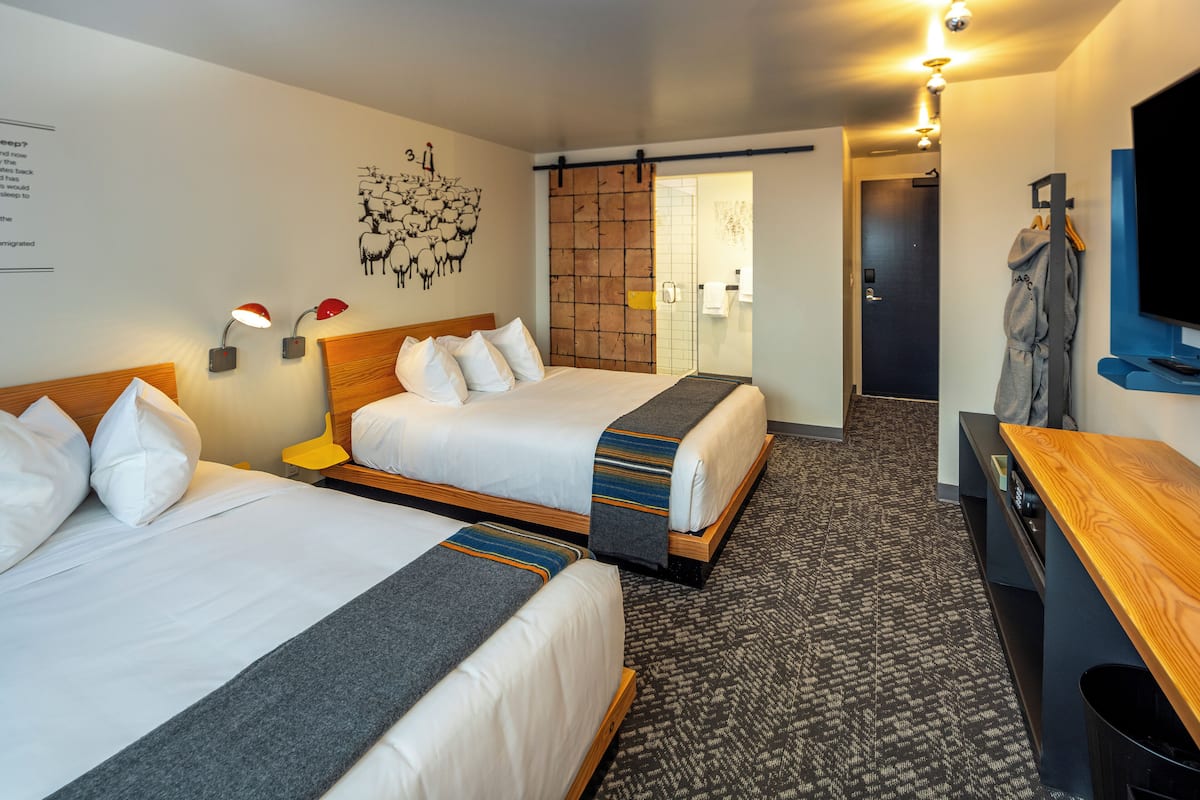 Quarto de hotel com duas camas, uma escrivaninha de madeira, televisão e chuveiro.