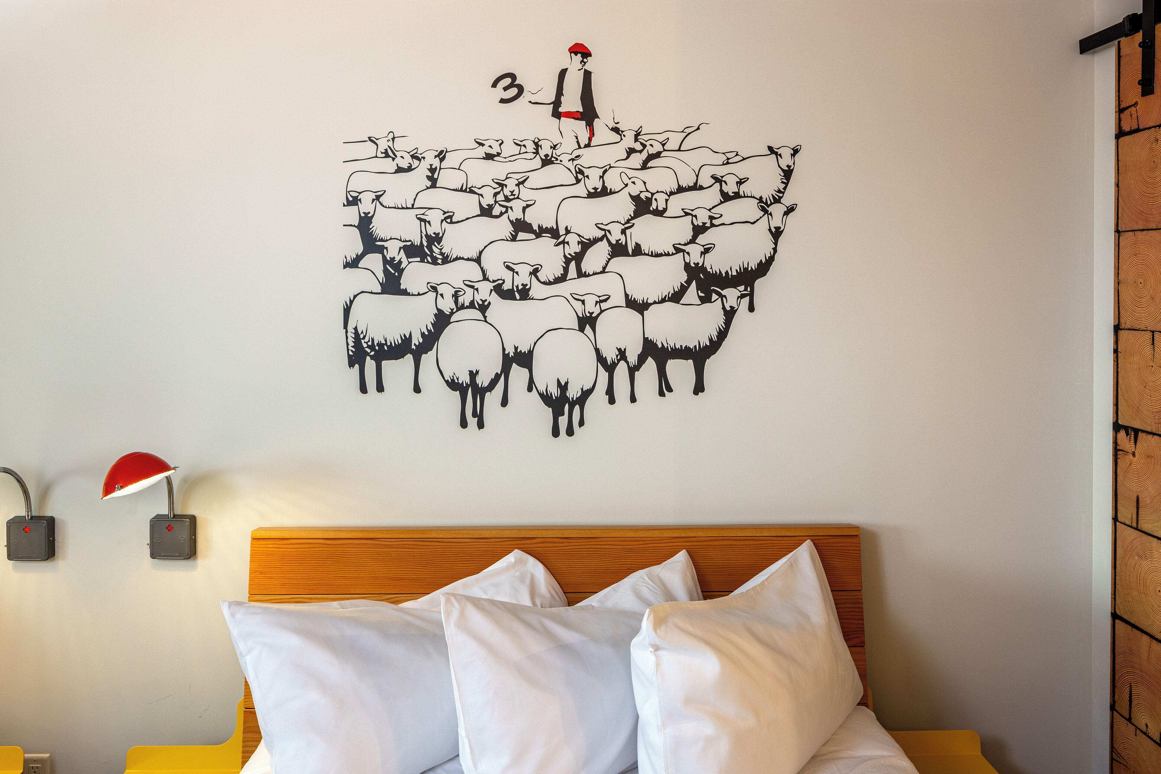 Een slaapkamer met een houten hoofdeinde, witte beddengoed en een muurdecoratie van een persoon die een kudde schapen leidt.