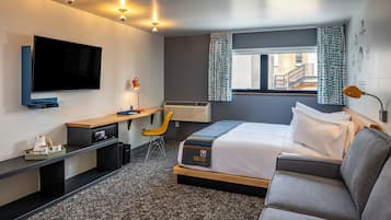 Una habitación de hotel moderna con una cama grande, un escritorio con silla, un televisor de pantalla plana y un ventanal con cortinas.