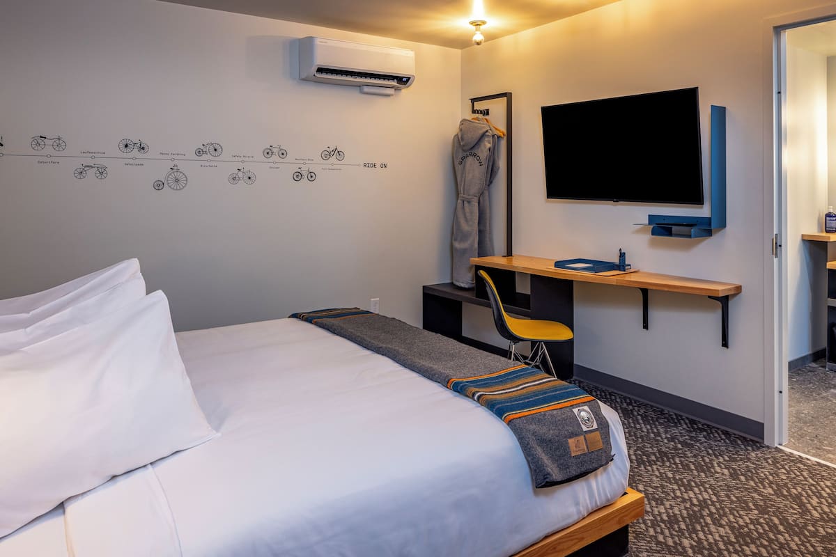 Quarto de hotel com cama, escrivaninha, cadeira, televisão e ar condicionado fixado na parede.