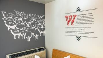Habitación de hotel con un mural que muestra una oveja contando, junto a un texto que explica su origen.
