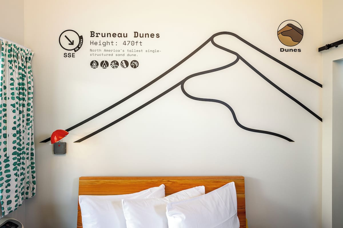 Uma parede com um mapa das Dunas de Brunei, uma cama com roupa de cama branca e um abajur vermelho.