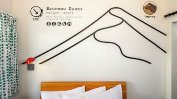 A wall with a map of Brunei Dunes, a bed with white bedding, and a red lamp.