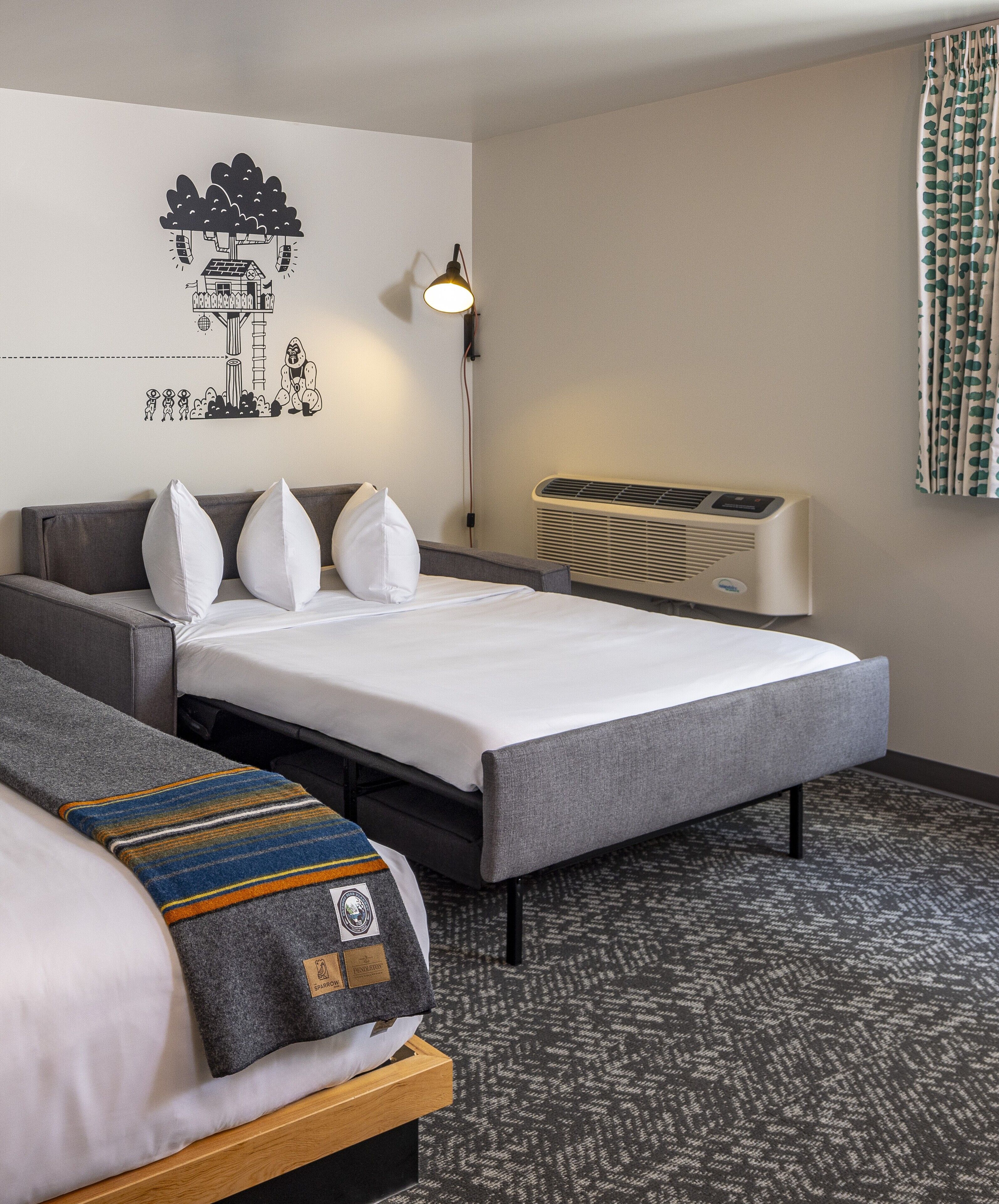 A hotel room with a bed, a sofa, a wall-mounted heater, and a wall decal.