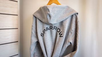 A grey hoodie with the word "SPARROW" printed on it, hanging on a wooden hanger.