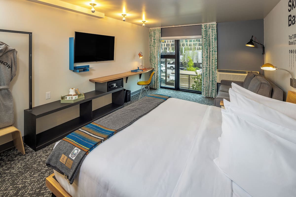 Quarto de hotel com cama, escrivaninha, televisão, cadeira e vista para o exterior.