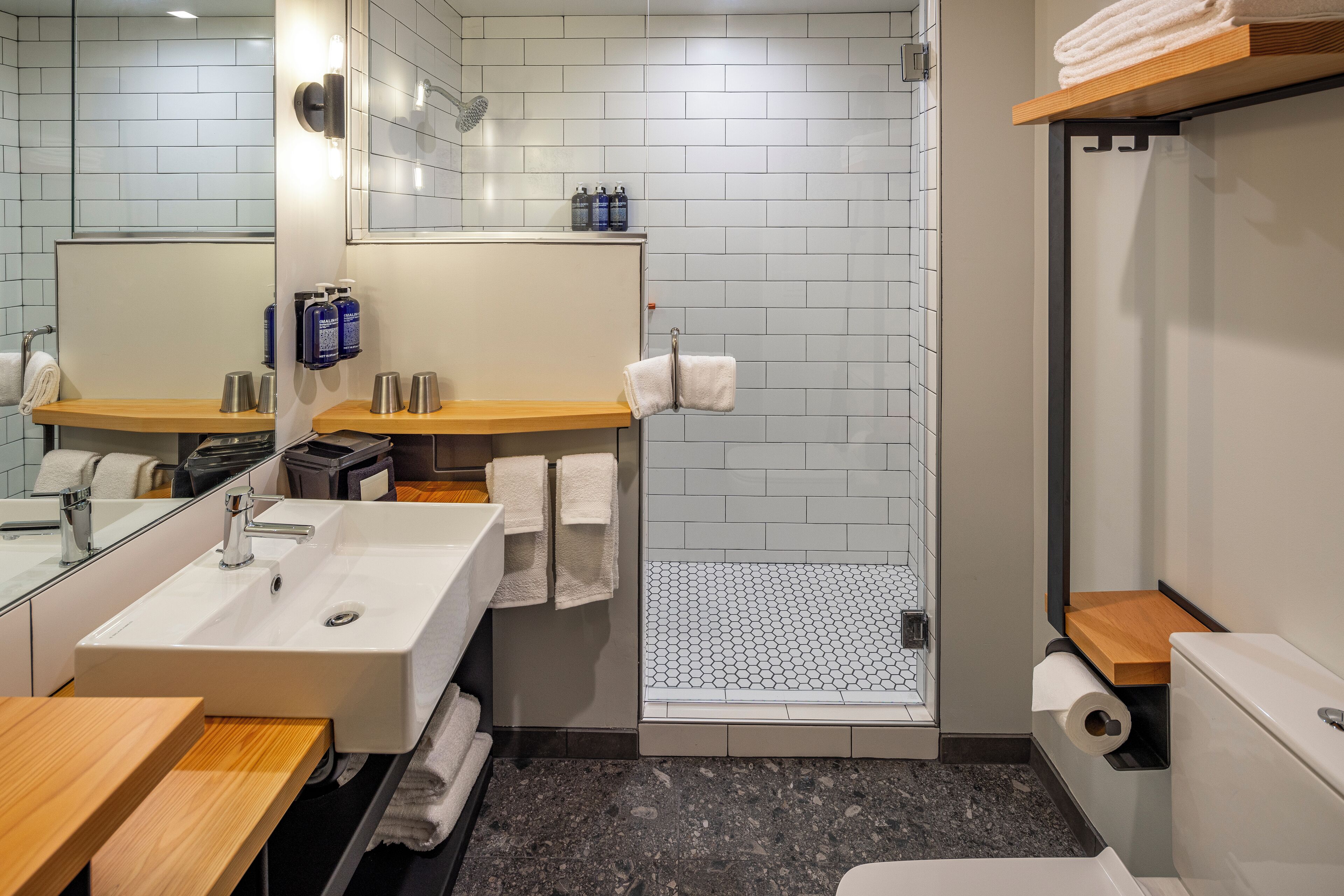 Une salle de bain moderne équipée d’un lavabo, d’un miroir, d’un porte-serviettes, d’une douche et de toilettes.