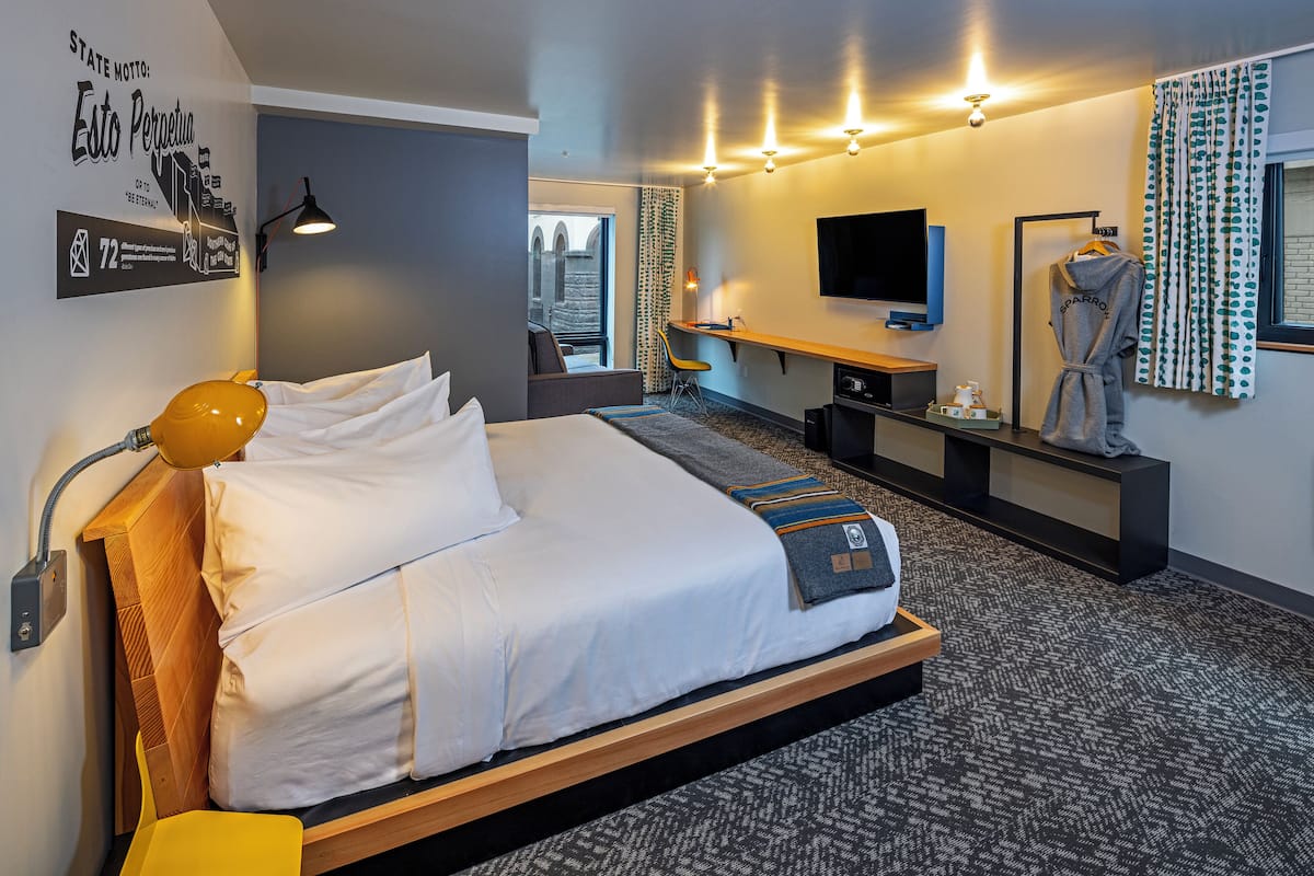 Quarto de hotel moderno com uma cama grande, uma escrivaninha, uma televisão e um roupão pendurado na parede.