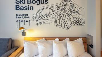 Una mappa a muro dei percorsi sciistici di Ski Bogus Basin, un letto con cuscini bianchi e un comodino con una lampada.