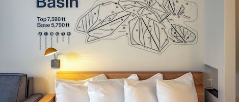 Een wandkaart van de skipistes van Ski Bogus Basin, een bed met witte kussens en een nachtkastje met een lamp.