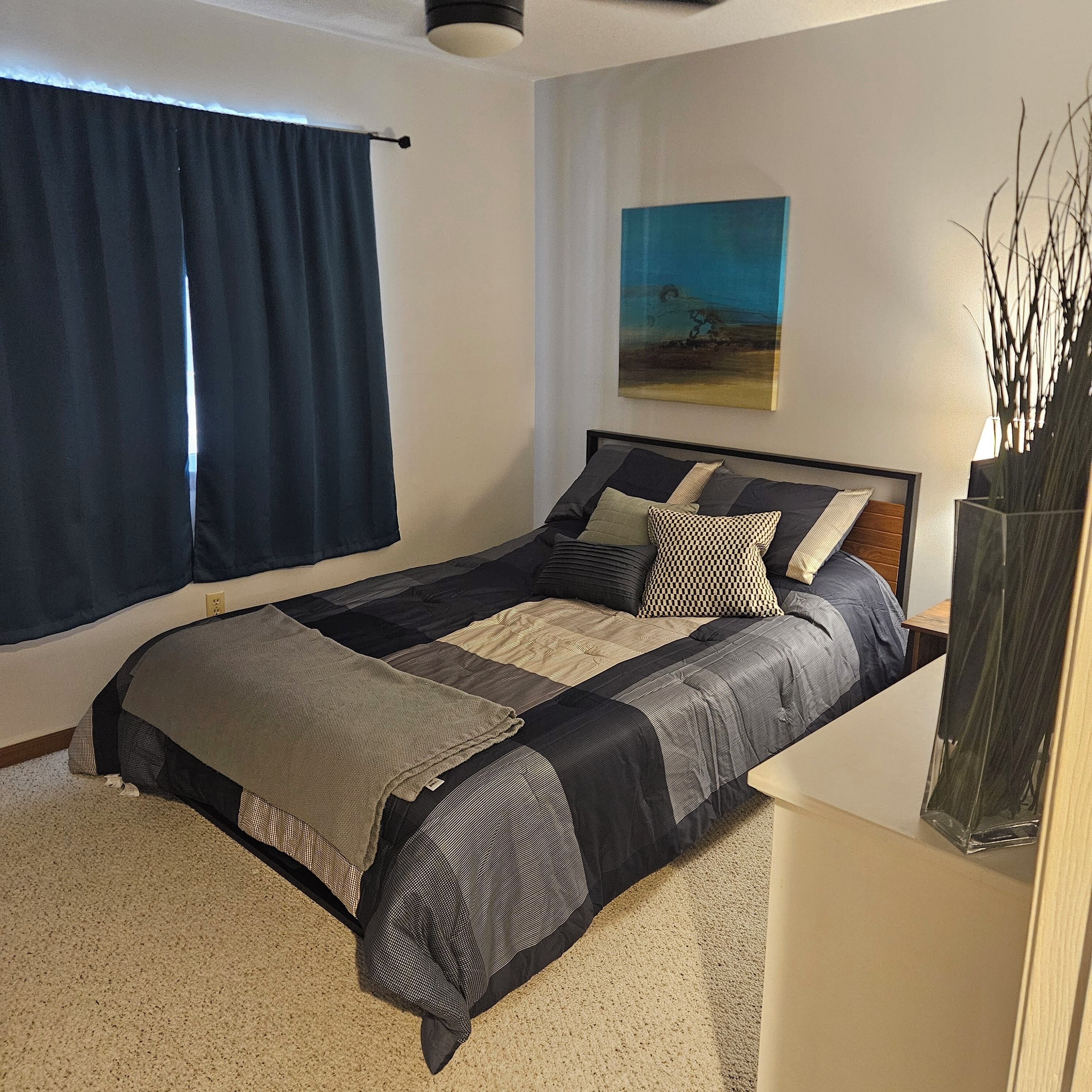 Un dormitorio con una cama, un cuadro y un florero con ramas.