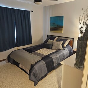 A bedroom with a bed, a painting, and a vase with branches.