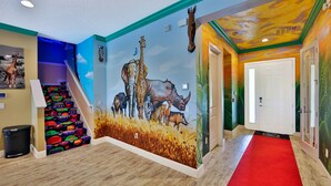 Un couloir orné d’une fresque colorée représentant la faune africaine, un tapis rouge et un escalier aux marches aux couleurs vives.