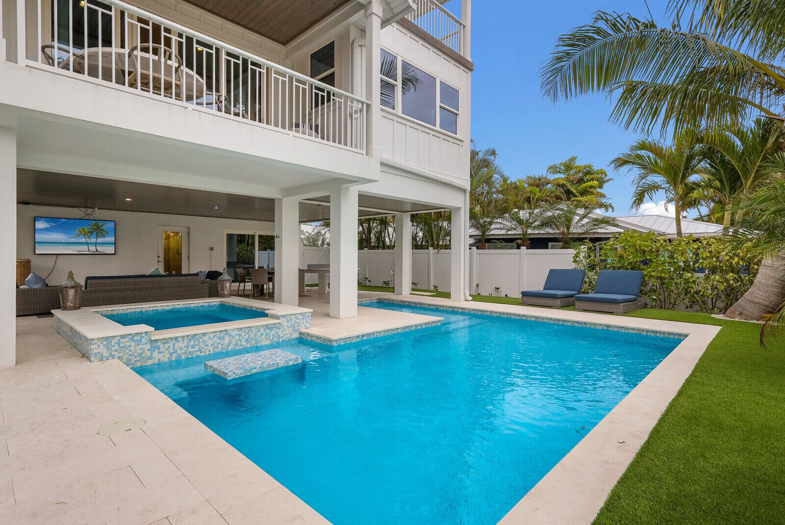 A two-story house with a swimming pool, outdoor seating, and a view of palm trees.