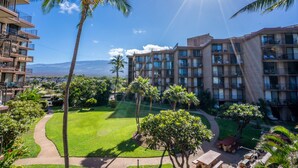 A hotel with multiple balconies, a well-maintained lawn, and palm trees. - 2 2 Oceanview Modern Resort Vistas (Kihei)