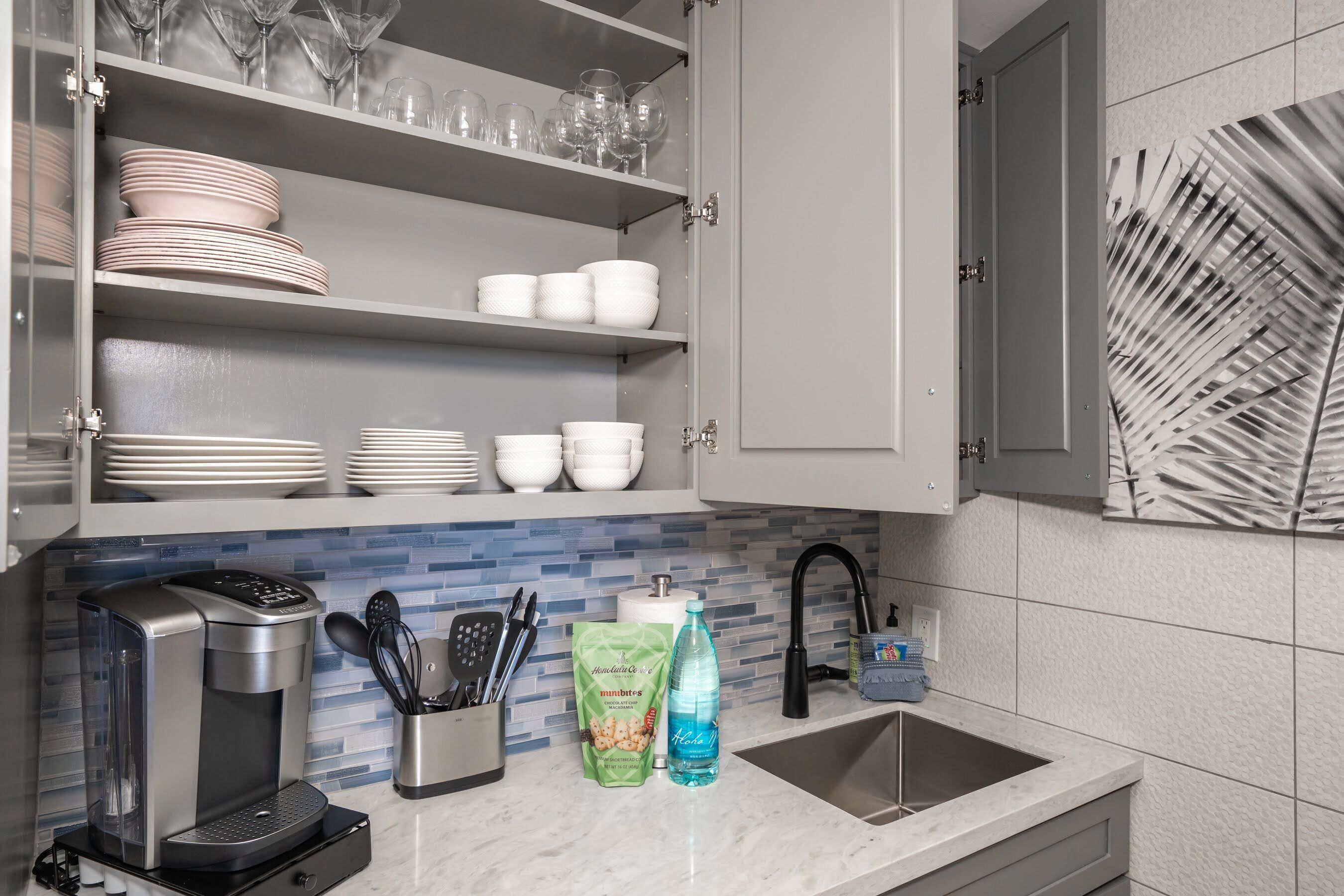 Una cocina con cafetera, un paquete de aperitivos y una botella de agua sobre la encimera.