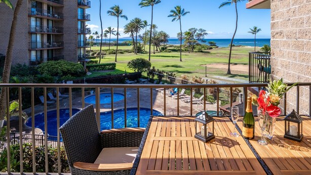 A balcony with a wooden table, a bottle of champagne, and a flower arrangement. - 2 2 Oceanview Modern Resort Vistas (Kihei)
