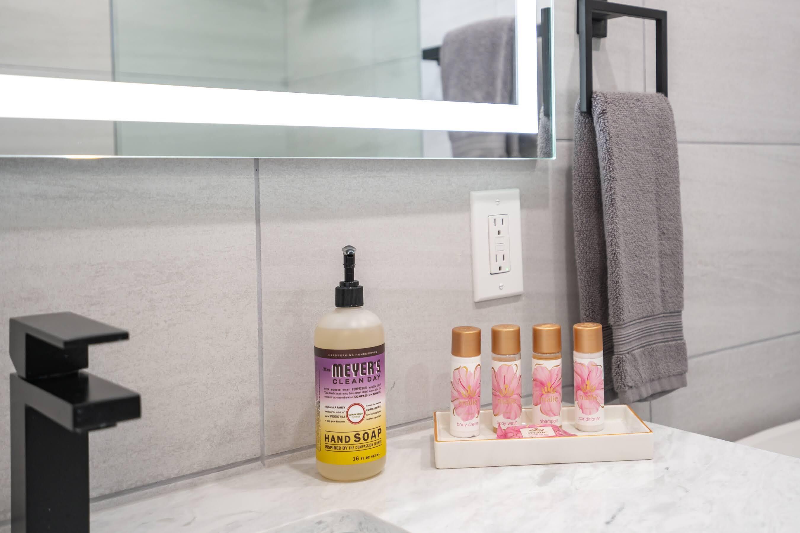 Un bagno con un moderno lavandino, una bottiglia di sapone mani e un vassoio con prodotti per la cura del corpo.