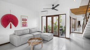 Ein modernes Wohnzimmer mit einem grauen Ecksofa, einem Holztisch und einem Deckenventilator.