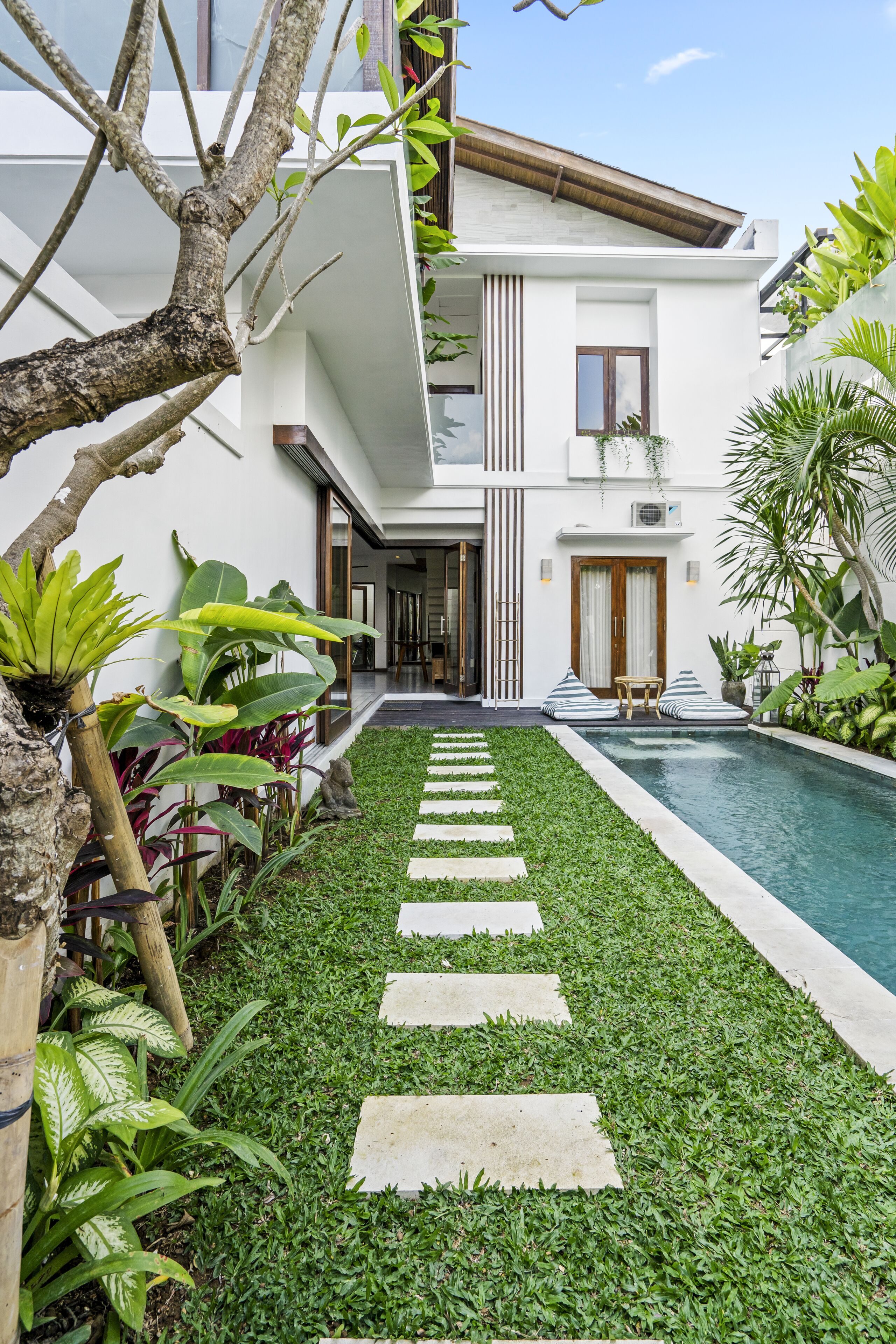 Une maison moderne dotée d’une piscine, d’une pelouse bien entretenue et de diverses plantes tropicales.