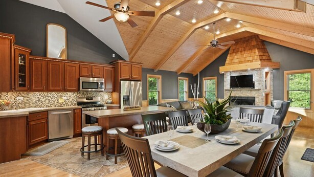 A spacious kitchen with wooden cabinets, a large island, and a dining area with chairs and a table set for six. - Modern, secluded luxury cabin near Castle Rock & Petenwell Lakes + Wisc. Dells (Necedah)