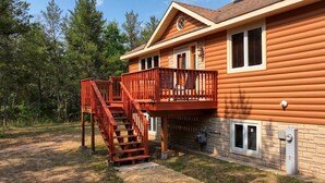 A two-story log cabin with a wooden deck and a staircase leading to an upper level. - Modern, secluded luxury cabin near Castle Rock & Petenwell Lakes + Wisc. Dells (Necedah)