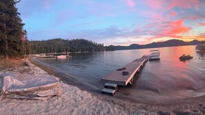 A lakeside scene with boats docked at a wooden pier, surrounded by trees and mountains in the background. - Priest Lake Waterfront Property With Majestic Lake & Mountain Views.

 (Coolin)