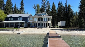 A waterfront property with a dock extending into clear water, surrounded by dense forest and featuring a large house with multiple decks and a covered patio area. - Priest Lake Waterfront Property With Majestic Lake & Mountain Views.

 (Coolin)