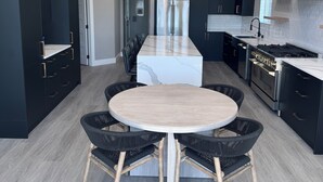 A modern kitchen with dark cabinetry, a central island, and a round dining table with chairs. - Priest Lake Waterfront Property With Majestic Lake & Mountain Views.

 (Coolin)