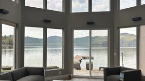 A spacious living room with large windows, a modern chandelier, and a view of a lake and mountains. - Priest Lake Waterfront Property With Majestic Lake & Mountain Views.

 (Coolin)