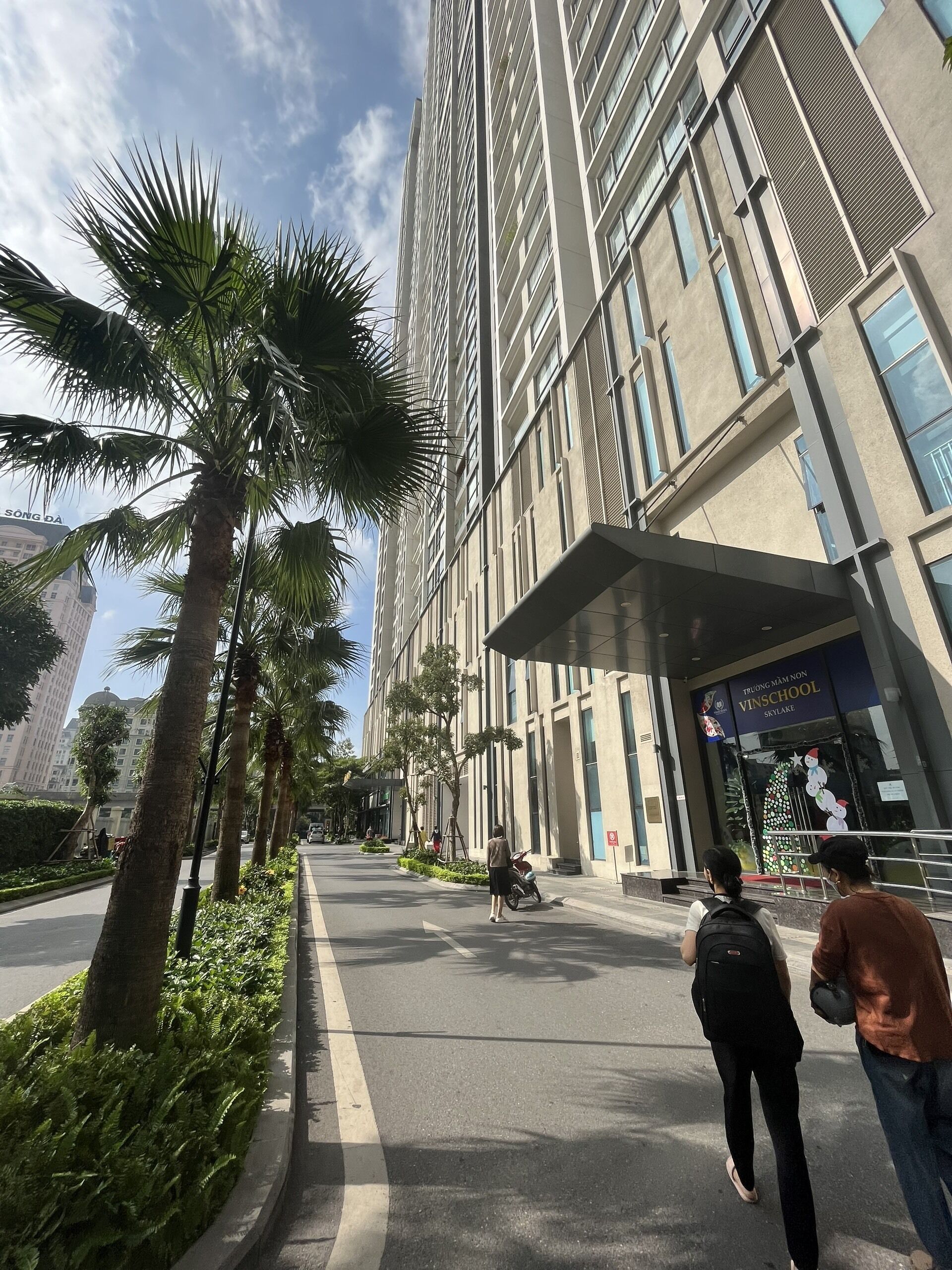 A modern building with a large entrance, palm trees, and a clear sky.