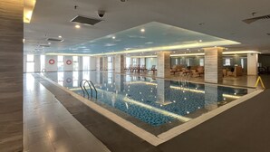 Piscina interior com água cristalina, rodeada por áreas de descanso e assentos.