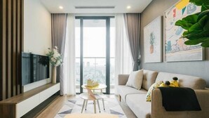 Uma sala de estar moderna com um sofá, uma televisão, uma mesa de centro e vista da cidade através de grandes janelas.