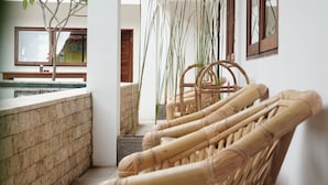 Un rincón de una habitación con un banco de piedra, una silla de mimbre y plantas altas.