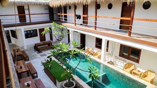 Zona de piscina con bancos de madera, una pequeña alberca y una estructura con techo de paja.