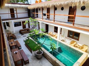 A poolside area with wooden benches, a small pool, and a thatched roof structure. - Gili Pirates (Gili Trawangan)