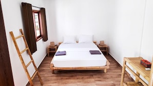 Una habitación pequeña y ordenada con una cama individual, mesitas de noche de madera, una pequeña mesa y una escalera.