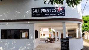 Un edificio con un cartel que dice "GILI PIRATES Dive Center Bed & Breakfast" y un panel de menú en el exterior.