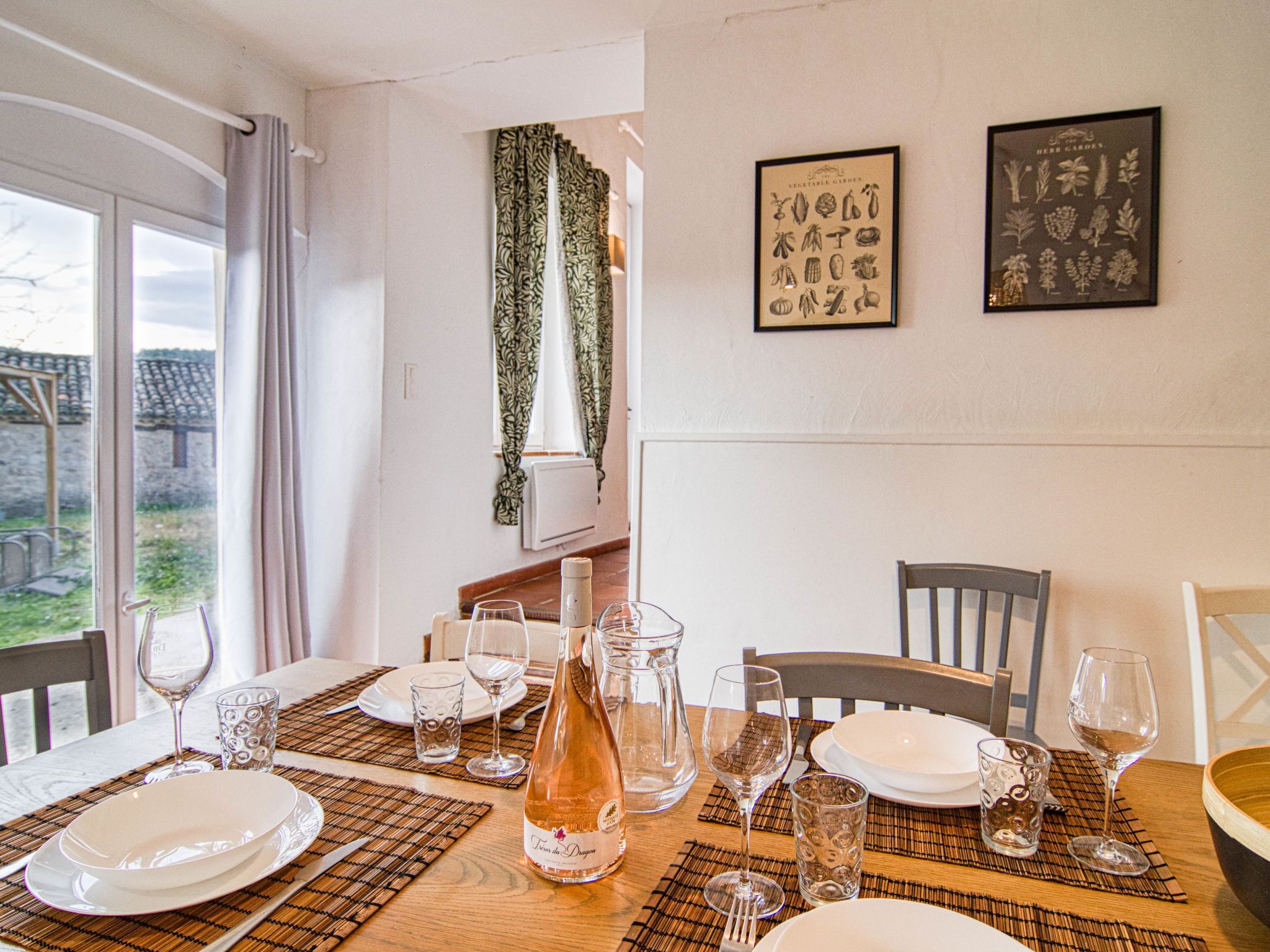 Een eettafel gedekt met borden, glazen en een fles, met uitzicht op het landschap door een raam.