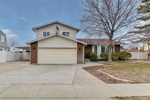 Une maison de plain-pied avec un garage, un petit jardin devant la maison avec un arbre, et un ciel dégagé.