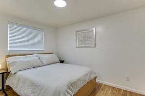 Une chambre à coucher avec un lit, une table de chevet, une fenêtre avec des stores et un tableau encadré au mur.
