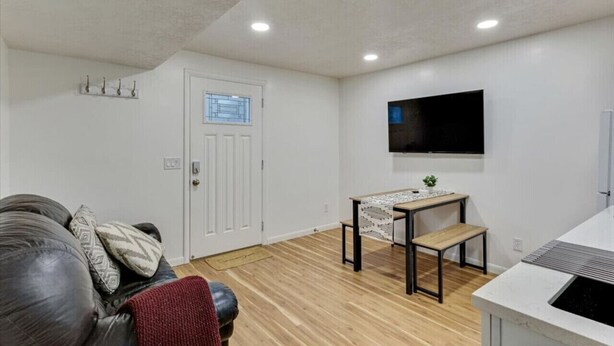 A living room with a sofa, a coffee table, a TV mounted on the wall, and a door with a window.