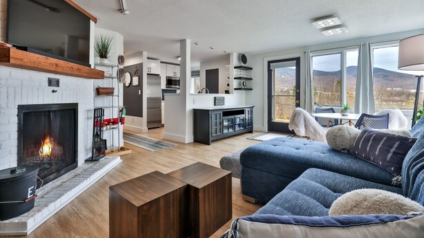A modern living room with a fireplace, a sofa, and a view of the mountains.