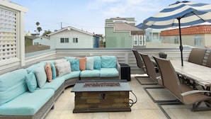 A rooftop patio with a curved light blue sofa, a stone fireplace, and a dining area with chairs and a table.