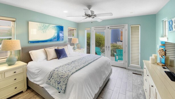 A bedroom with a bed, nightstands, a ceiling fan, and a view through glass doors to an outdoor area.