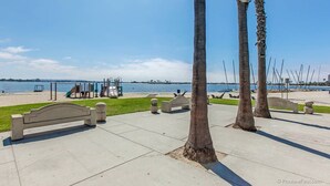 Un parc avec une aire de jeux, des bancs et des palmiers, situé au bord d’un plan d’eau.