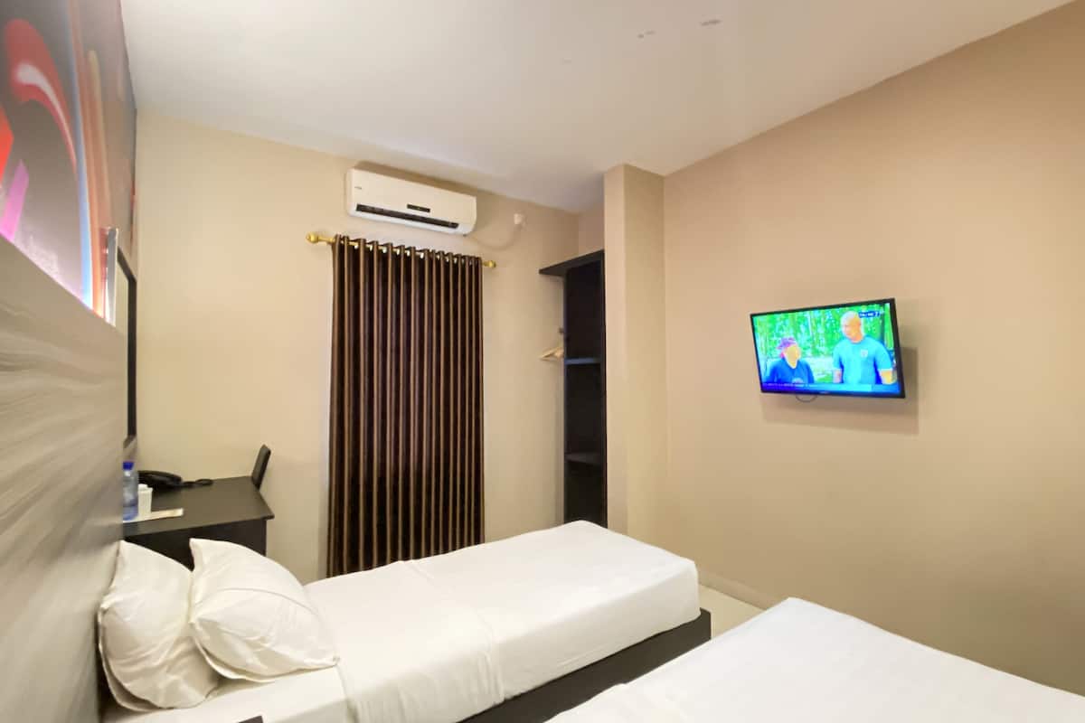 A hotel room with a bed, a desk, a chair, an air conditioning unit, a television, and a curtain.