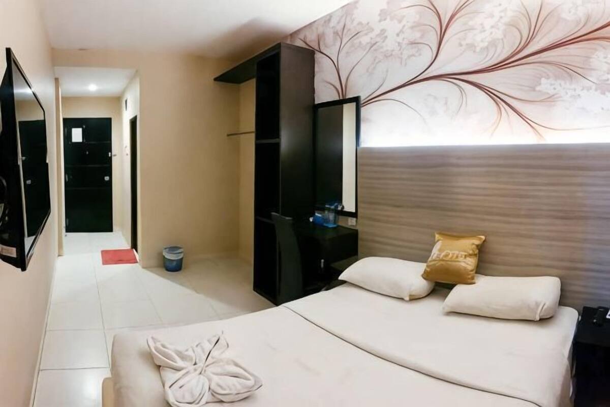 A hotel room with a bed, a desk, a mirror, and a door leading to another room.